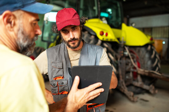 Two mature male farmers discussing work with tablet in barn