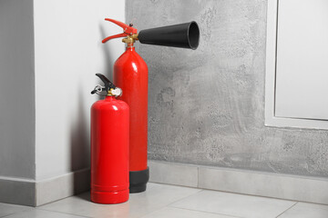Fire extinguishers on floor near grey wall indoors