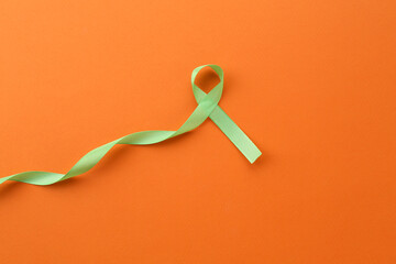 Light green awareness ribbon on orange background, top view