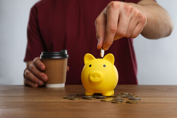 Man putting coin into yellow piggy bank at wooden table, closeup