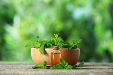Bottle of mint essential oil and fresh leaves on wooden table