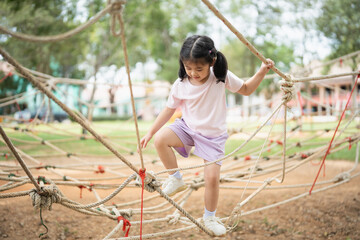 Asian young girl is playing on a rope course, climbing up and down the ropes. The scene is lively and playful, with the girl enjoying herself as she navigates the course