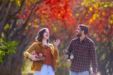 Obraz premium Happy caucasian farmer couple carrying organics homegrown produce harvest with apple and firewood while walking along the country road with fall color from maple tree during autumn season