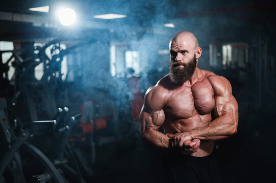 Muscular bald man posing shirtless. Bodybuilder showing off his shape in the gym.