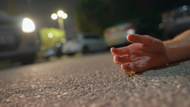 Dead man. Hand falling on the road. Person shot down hurt or past out after fighting crime. Police lights reflecting on the Ground with Flashing hand on the ground. getting a bullet. suicide.