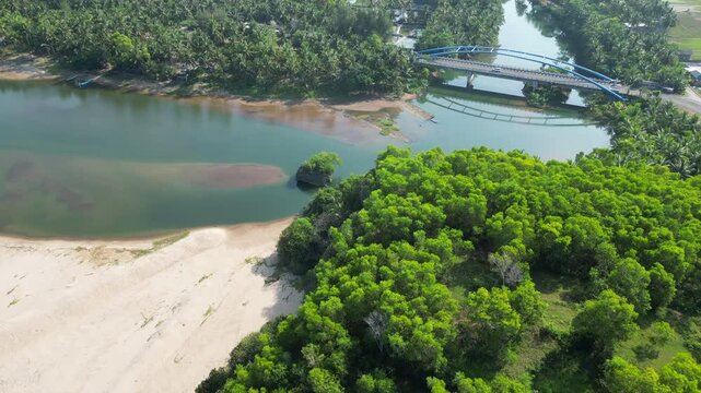 Cars Cross Bridge As Drone Descends Over Rich Jungle And Blue River Leading To Pantai Soge Beach Java Indonesia