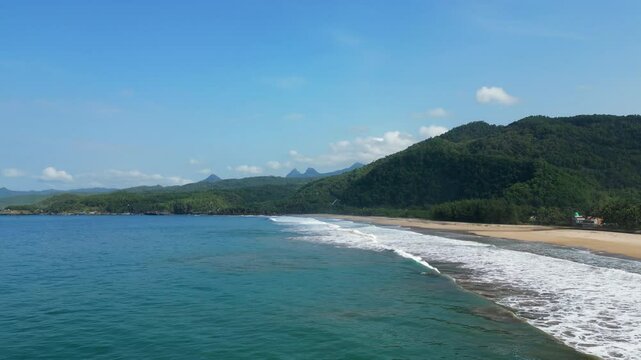 Blue Waves Roll Into Pantai Soge Beach In Java Indonesia With Jungle Covered Mountains In Background