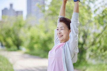 春の新緑の中ストレッチをを行うスポーツウェアをきたシニア女性