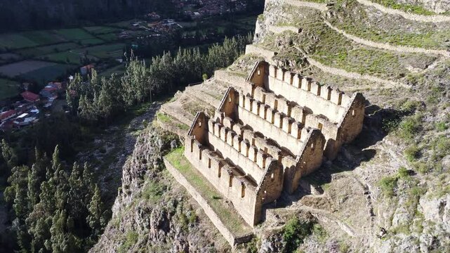Aerial high angle pan left of historic town site of Ollantaytambo cut out of hillside in Peru