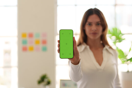 Young woman in office holding mobile phone showing green screen