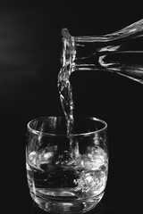 a vessel pouring water into a glass, black background