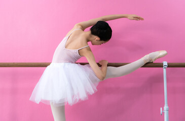 A girl ballet student practices ballet dancing at home with a pink and white background