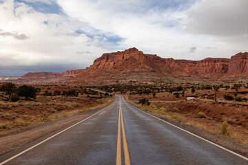 A picturesque road leading into the stunning red rock formations of Zion National Park, Utah, with an expansive sky above and rugged terrain on either side, showcasing nature's raw beauty.
