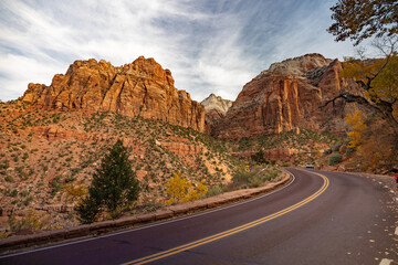 A winding road curves through the stunning rock formations of Zion National Park in Utah under a partly cloudy sky