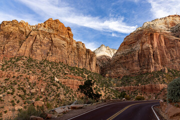 The aweinspiring view of rugged cliffs and picturesque roads in Zion National Park, Utah, under a sunny sky with wispy clouds is truly breathtaking and motivating for exploration and adventure