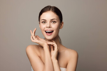 Beautiful young woman posing with her hands on her face and looking at the camera, on a gray background