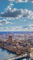 Fototapeta premium Beautiful vertical panoramic view of Westminster Abbey, Big Ben, House of Parliament and the River Thames at sunset with the city of London to the horizon under a sunny sky with backlit white clouds.