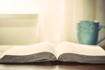 Fototapeta premium close up of open bible with a cup of coffee for morning devotion on wooden table with window light, christian background