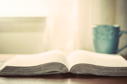 close up of open bible with a cup of coffee for morning devotion on wooden table with window light, christian background

