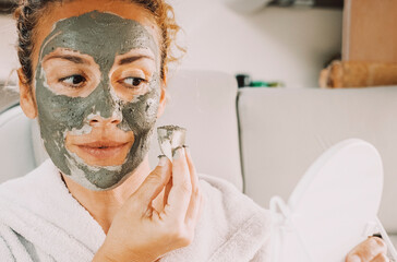 Portrait front view of young woman with skin cream treatment on face inside a camper van. Beauty anti aging mud on female people. Lady using natural skin care product looking on a mirror. Youthful