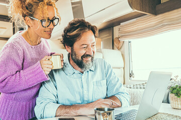 Happy couple man and woman working and using together a laptop computer inside a camper van planning holiday vacation destination and living vanlife lifestyle in freedom. People travel and tourism