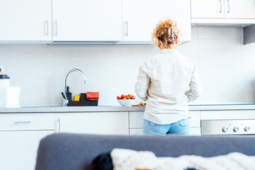 Back view or real woman working in the kitchen at home in indoor leisure activity. White house ambient minimal style. Female people lifestyle independence life