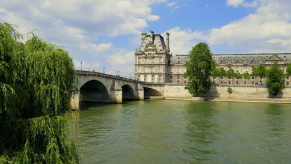 Fototapeta premium imposantes Rathaus von Paris am Ufer der Seine mit alter Bogenbrücke unter blauem Himmel