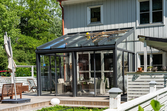 The glass house is attached to the wall of large house. The recreation area is inside of greenhouse. Outdoor furniture, table and chairs in the glass terrace. Design concept interior villa courtyard