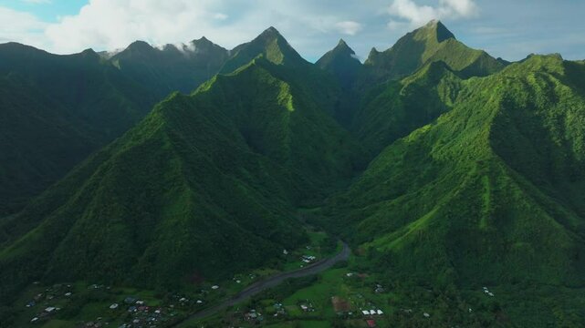 Late afternoon sunset green island mountain peaks Teahupoo Tahiti French Polynesia aerial drone town village Paris summer Olympics venue Mount Orohena Aorai Ronui blue sky river valley forward pan up