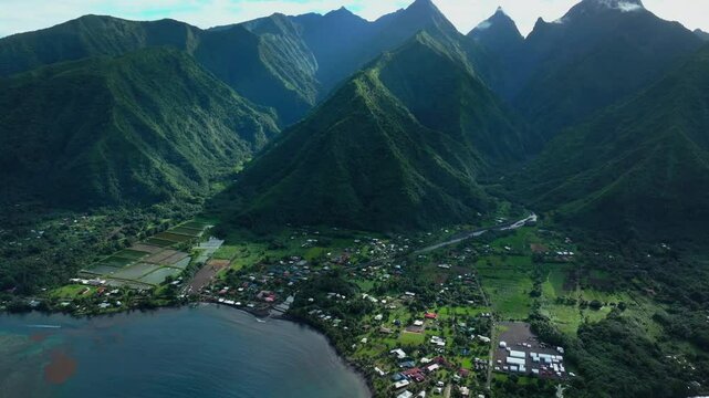 Teahupoo Tahiti French Polynesia aerial drone sunny morning shade green island mountain peaks  town village Paris summer Olympics venue Mount Orohena Aorai Ronui blue sky river valley forward pan up