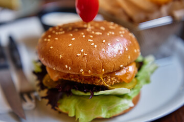 Close-up of tasty chicken burger with side of crispy fries in basket served on white plate in restaurant. Fast food and junk food concept