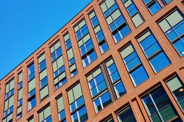 Modern office building with brick facade and large windows reflecting clear blue sky. Contemporary urban architecture