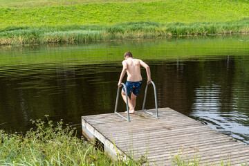 Young man guy going to swim in the lake. Special wooden pier is equipped with steps into the water. Young male swimmers on summer holidays fun enjoy relax his outdoor activity recreation.