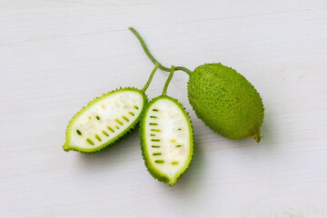Sliced and whole spiny gourd green vegetable on light white wooden background. Momordica dioica is...