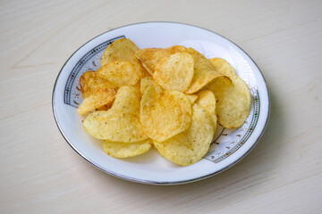 Potato chips on a white plate on wooden background. Crunchy delicious lays potato chips, American style cream and onion flavor.