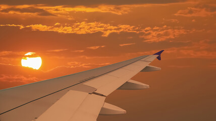 Image of aircraft wing flying in the dramatic atmosphere of sunset sky with part of the sun could be seen behind the clouds.Image use for transportation industry and travel business background.