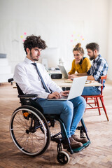 Young man in wheelchair working with colleagues on a new project in a startup company office. Working in co-working space.