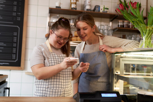 Smiling cafe owner with down syndrome learning cash register in coffee shop