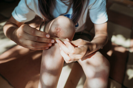 Hands of girl applying bandage on wounded leg