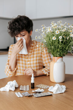 Woman with flower allergy blowing nose sitting at home