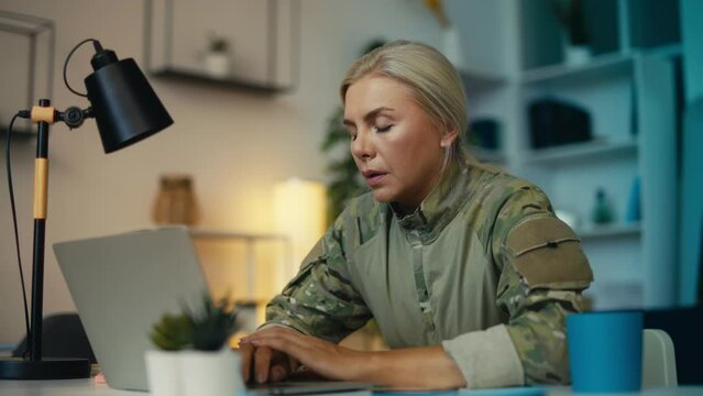 Tired female military officer works on laptop in office, frustrated with her job