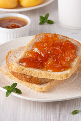 Apricot jam on bread in a white plate and a jar of apricot jam
