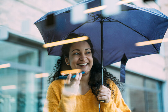 Happy businesswoman holding umbrella and talking through speaker phone