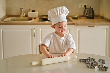 A young child wearing a chef's hat is rolling out dough on a table