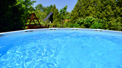 Swimming pool with metal frame for home and garden. Frame swimming pool in the yard. Garden in the background. Summer holiday fun and recreation.