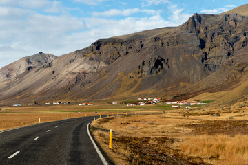 a road crossing yellow grass meadows in Iceland. A range of volcanic rock can be seen in the background.