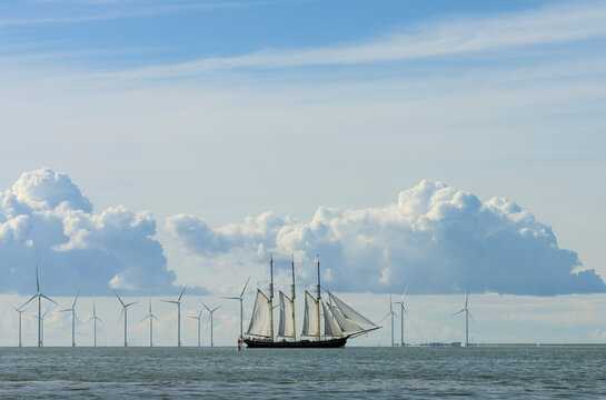 Sailboat sailing near wind turbines under cloudy sky in sea