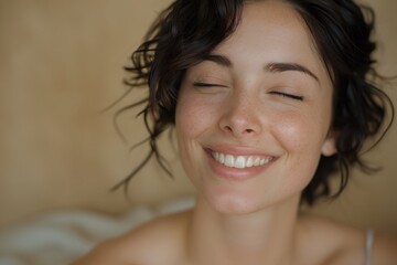 Close-up of a smiling woman with closed eyes, exuding happiness and serenity, against a neutral background.