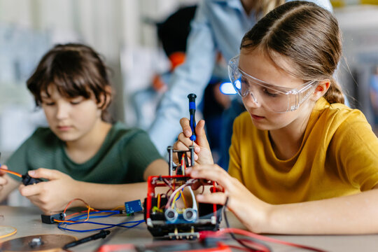 School girls working on circuit board of small robot, building robotic car in after-school robotics club. Children learning robotics in Elementary school. Girls in science.