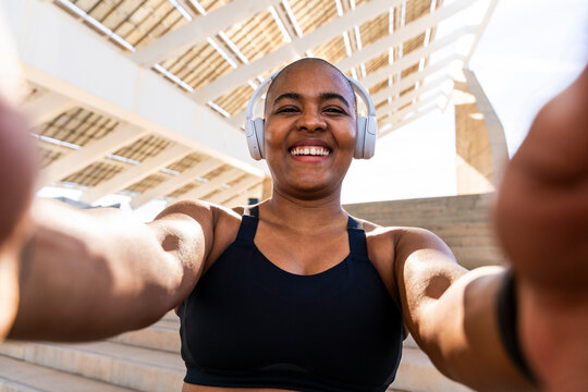 Happy sporty woman wearing headphones taking selfie on sunny day